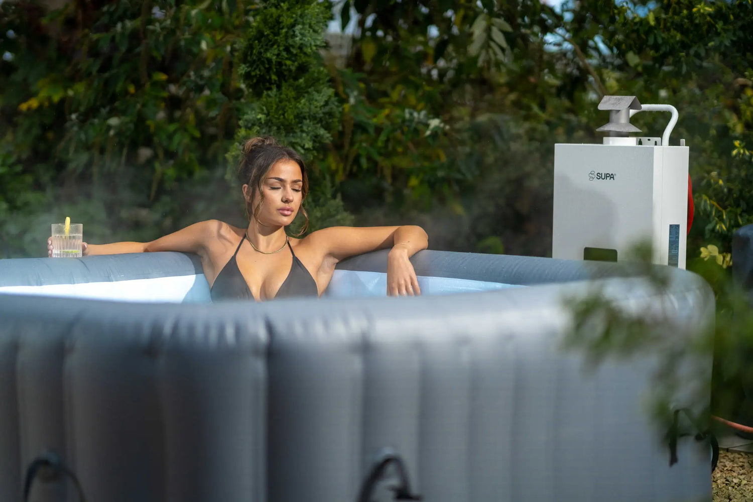 Woman relaxing in an inflatable hot tub outdoors with a tree in the background